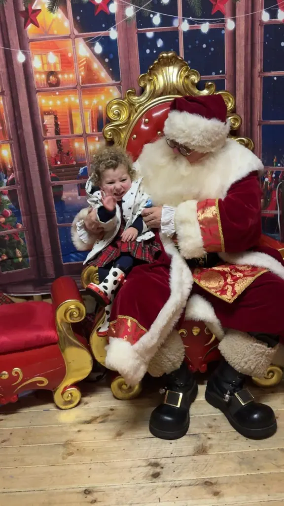 A young child sitting with Father Christmas on his golden chair